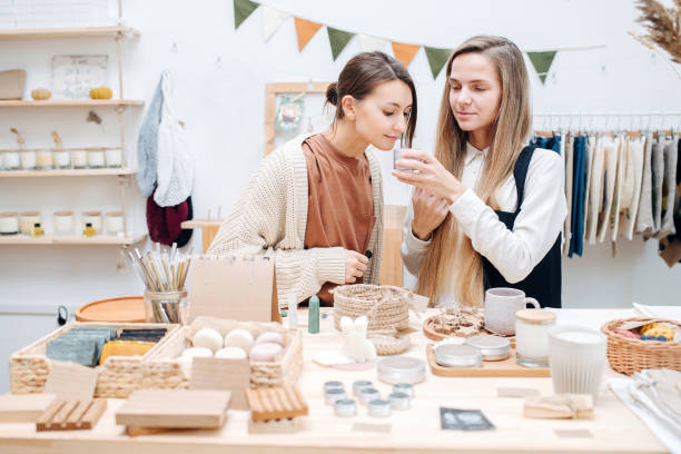 Social curious young women in an ecological shop choosing between various cosmetic products. One giving another a plastic jar to smell a product inside.