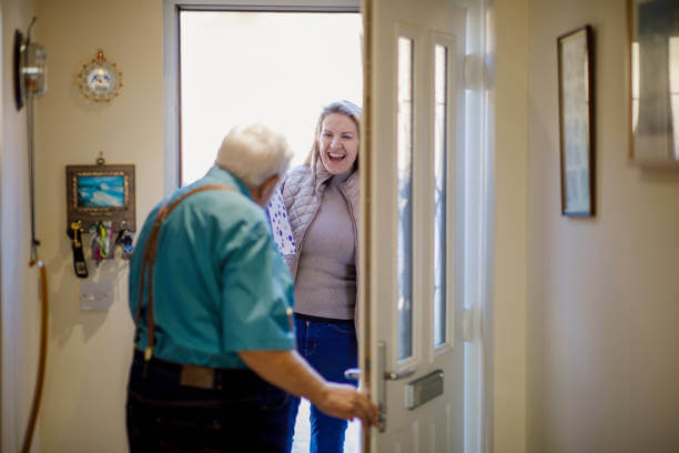 Caucasian senior male opening the front door to his daughter holding a gift.