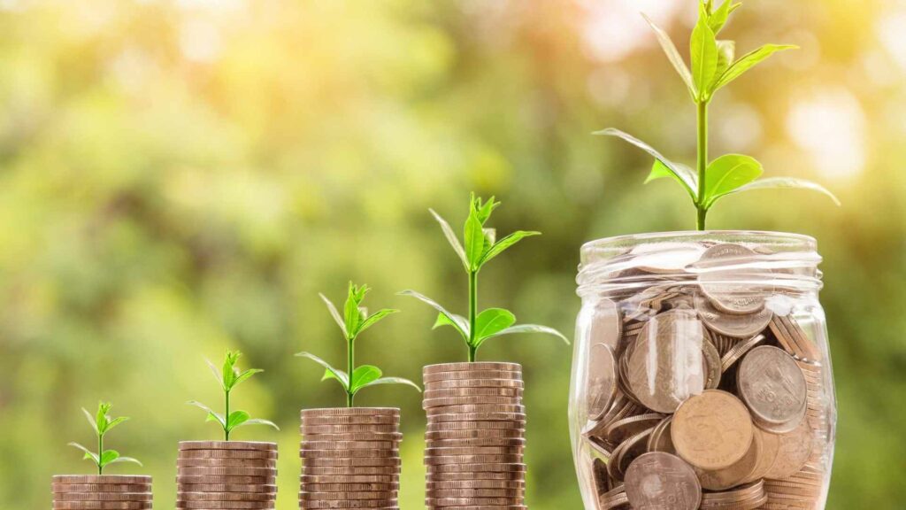 How to Grow an Affiliate Marketing Business - Small seedings growing from a stack of coins and a coin jar.