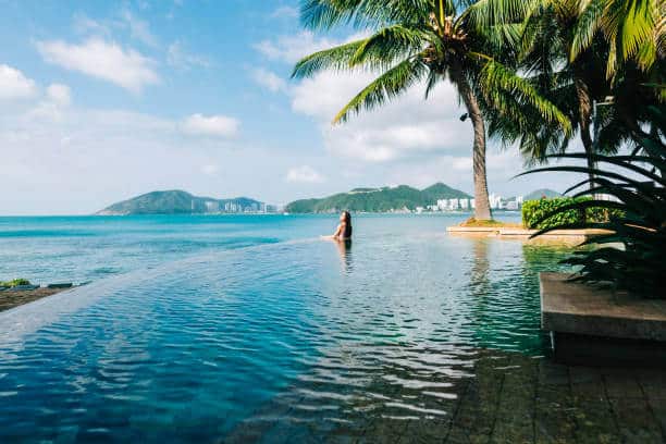 Young caucasian woman in swimming pool on beautiful tropical bay, blue sky and ocean, summer vacation