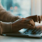 Close up of a mans hands typing on a laptop.