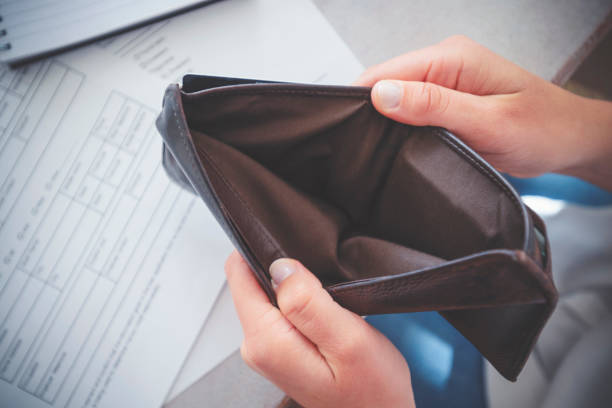 Woman opening an empty wallet. There is paperwork on the desk in the background. Poverty, budget and overspending concept.