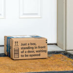 General view of an Amazon shipped cardboard box package with "just a box, standing in front of a door waiting to be opened" on the doorstep of a suburban home in Spokane, Washington