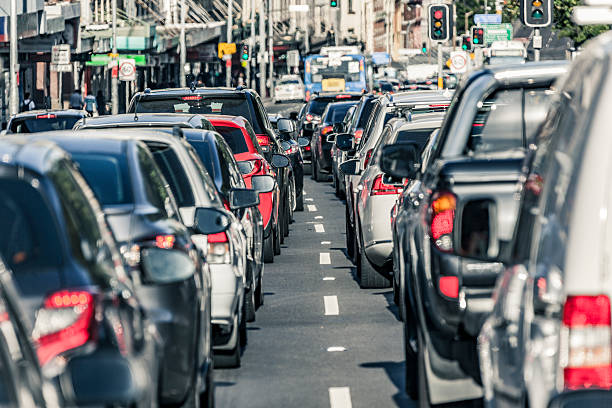 Rush hour traffic gridlock on busy Sydney main road.  Looking between two lanes of stationary vehicles with brake lights illuminated plus both red and green traffic lights.  A public transport bus is in the distance.  Horizontal, heat haze (shimmer).